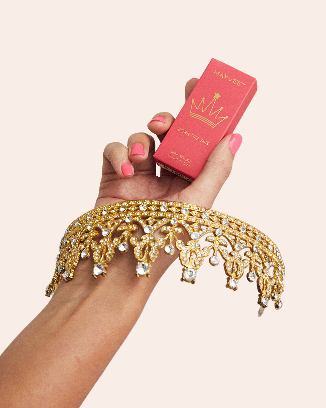 A hand with pink nail polish holds a small red box labeled MINCVEX while wearing a wide gold crown headband embellished with clear rhinestones. The background is a solid pale beige.